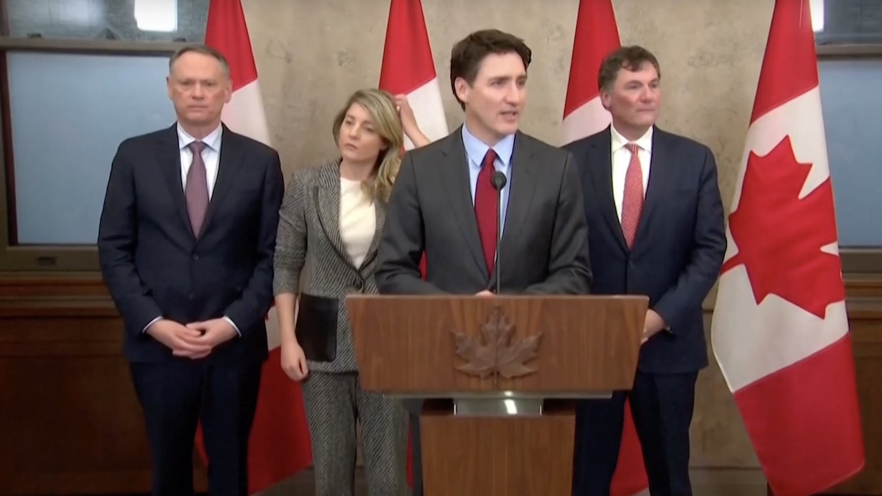 Canadian Prime Minister Justin Trudeau, flanked by officials, speaking at a press conference to announce retaliatory tariffs on U.S. goods amid escalating trade tensions.